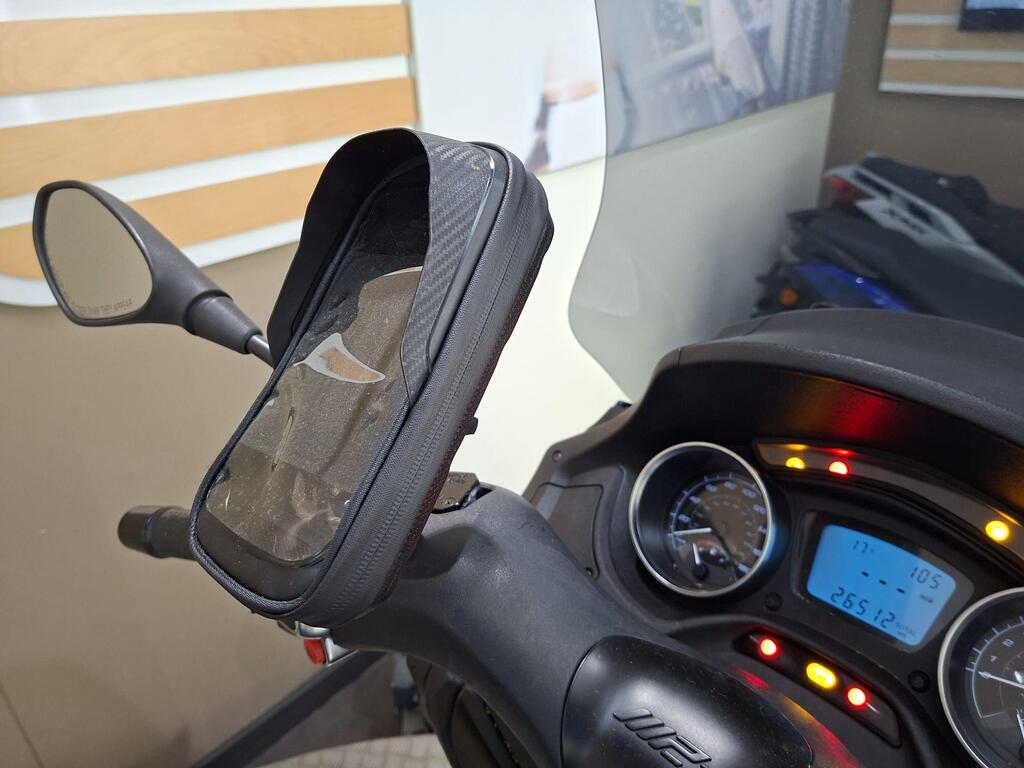 Piaggio MP3 350 2019 18 A close-up of a motorcycle handlebar featuring a phone mount, side mirror, and a digital dashboard displaying information like speed and mileage.