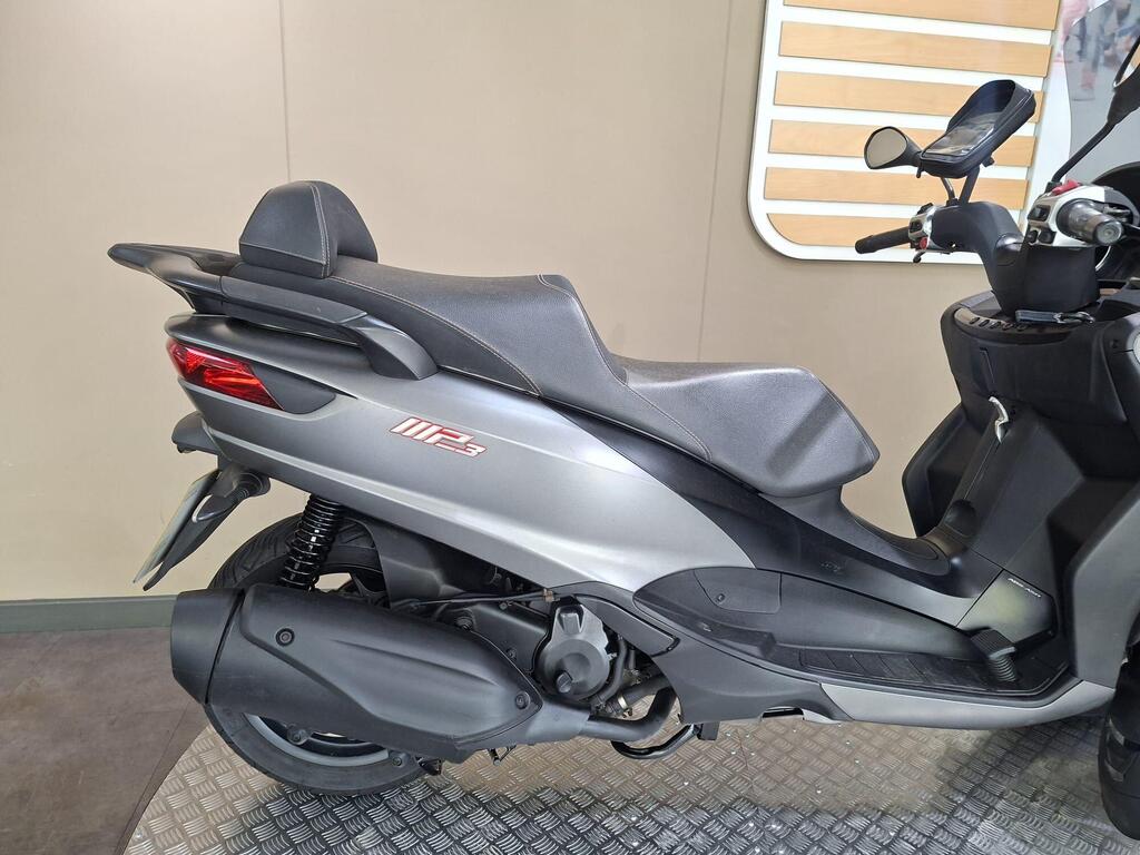 Piaggio MP3 350 2019 21 A grey scooter parked on a textured floor, showcasing its streamlined design and dual exhaust on the left side.