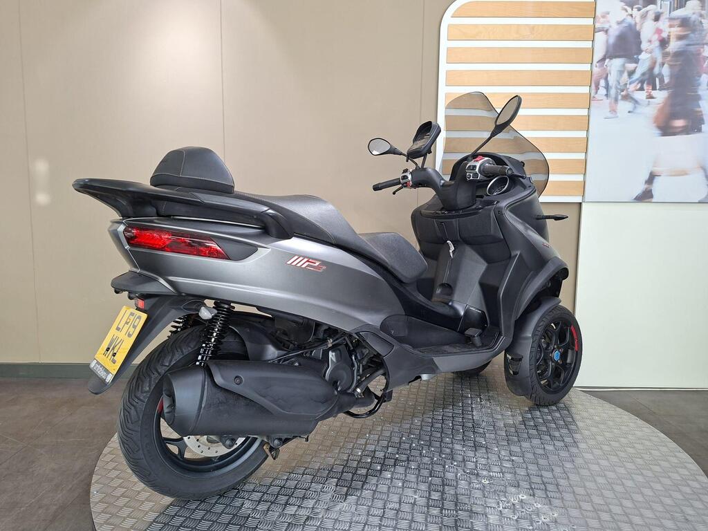 Piaggio MP3 350 2019 5 A black three-wheeled scooter with an ergonomic seat and a prominent rear light, positioned on a textured display surface, with a neutral background.