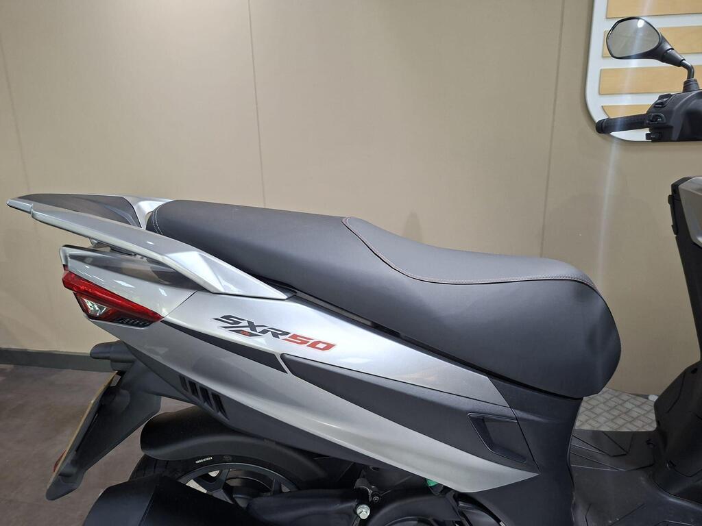 Aprilia SXR 50 2026 18 Close-up of the seat and rear section of a silver and black scooter, showcasing the "SXR50" model name and streamlined design elements against a neutral background.