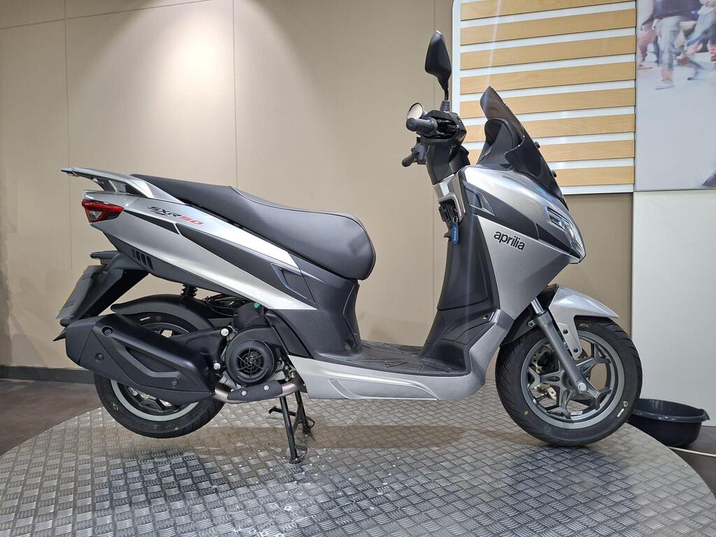 Aprilia SXR 50 2026 21 Aprilia SXR 50 2026 A silver Aprilia scooter displayed on a textured surface against a neutral background.