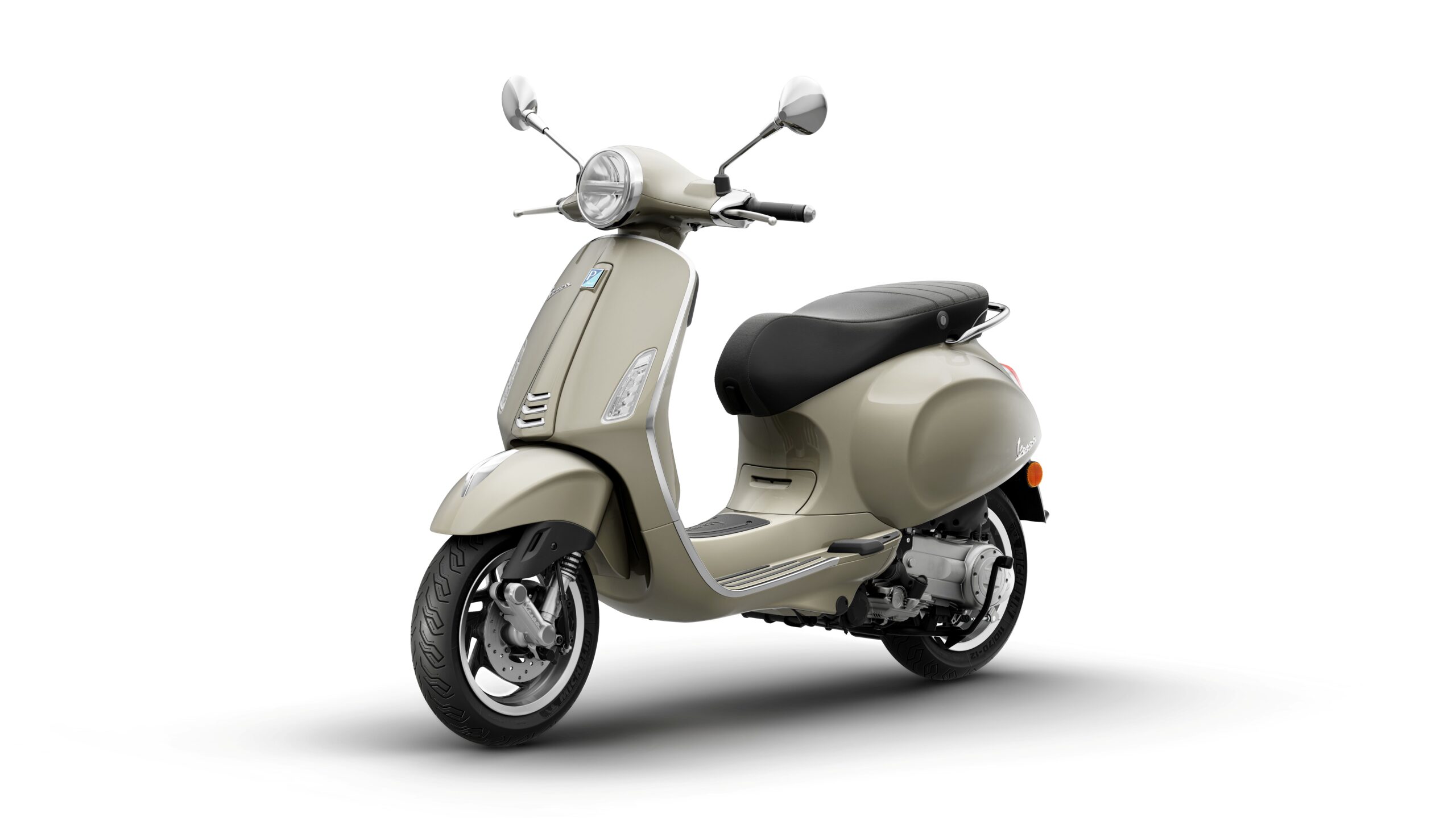 Vespa Primavera 50 MY26 Beige Avvolgente Lateral Left A stylish beige scooter with a black seat, chrome accents, and a vintage design, positioned at a slight angle on a white background.