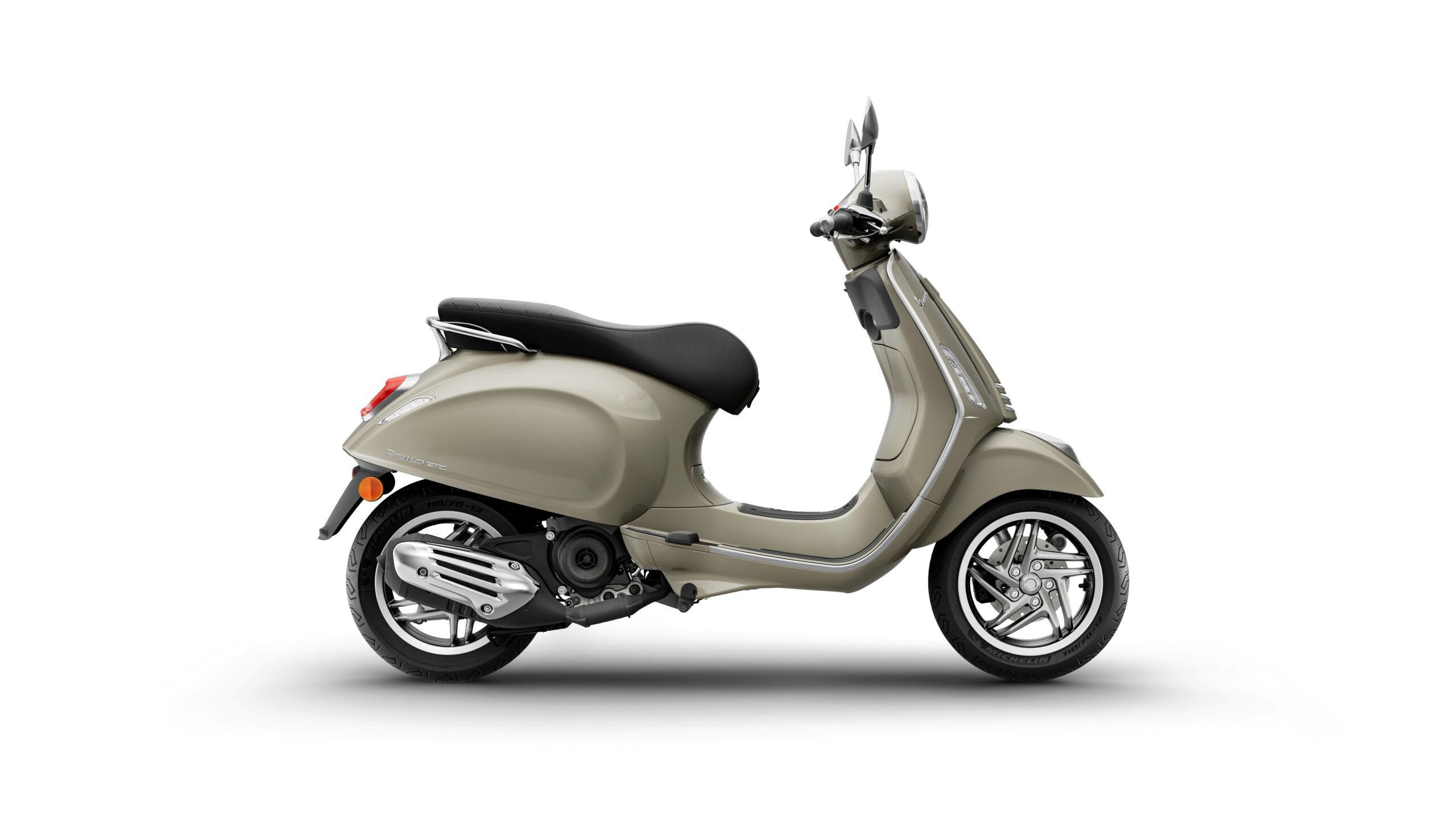 Vespa Primavera 50 MY26 Beige Avvolgente Right A side view of a sleek, beige scooter with a black seat, featuring chrome accents and stylish wheels, set against a white background.
