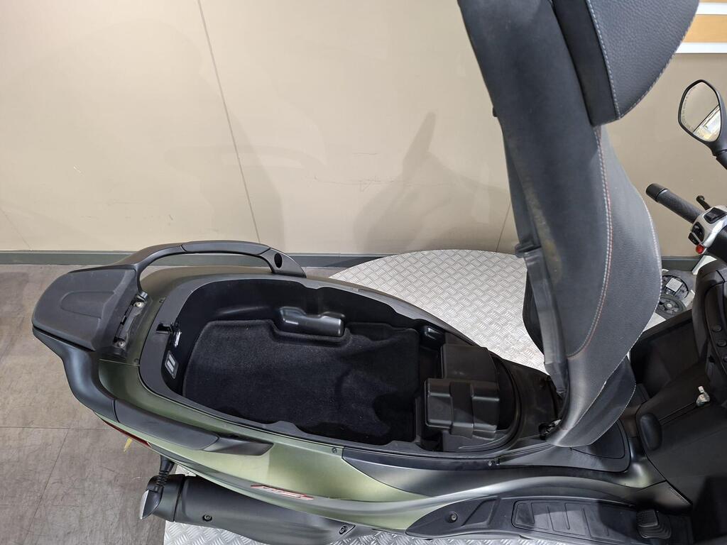 Piaggio MP3 350 LT Sport 2020 11 A top-down view of a scooter with the seat raised, revealing a storage compartment beneath. The interior is dark with a black carpet lining, and the scooter's body is a sleek green color.