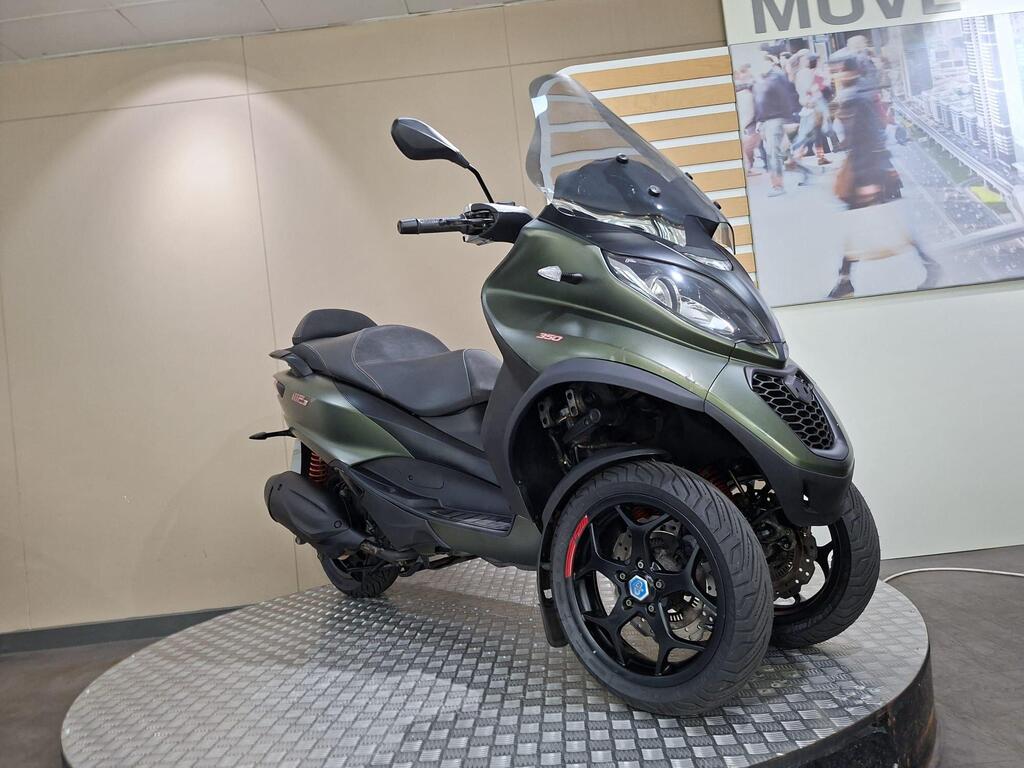 Piaggio MP3 350 LT Sport 2020 3 A green three-wheeled scooter displayed on a circular platform, with a transparent windscreen and modern design elements, set against a neutral background.