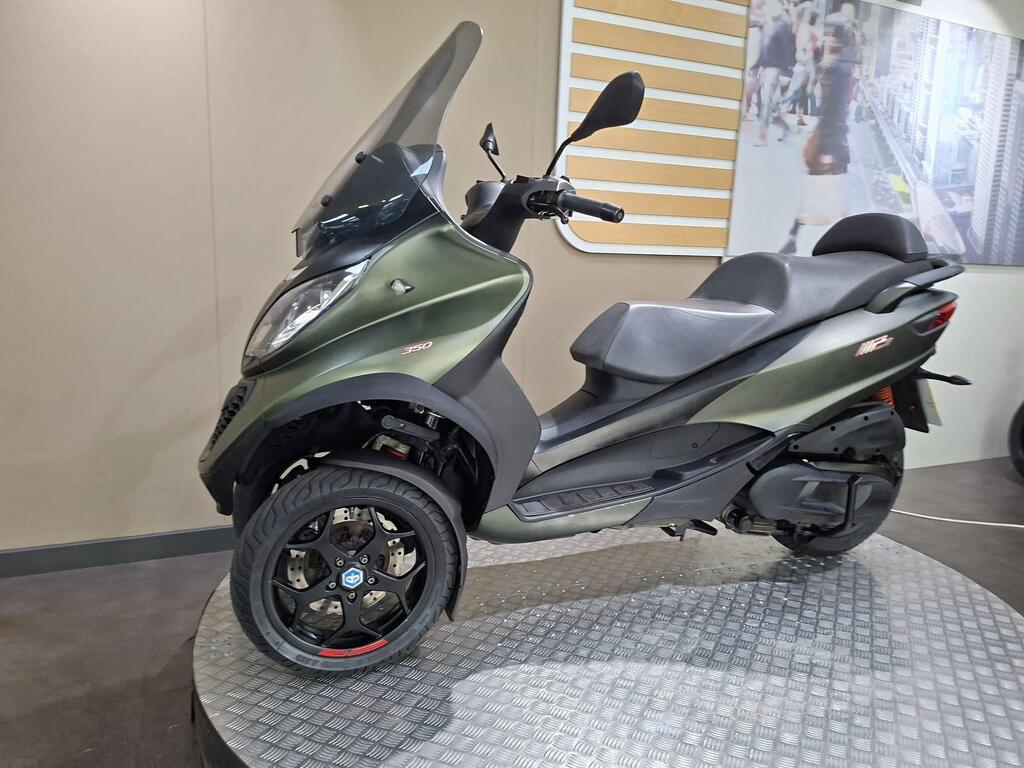 Piaggio MP3 350 LT Sport 2020 8 A green three-wheeled scooter with a windshield and black wheels on a round display platform, set against a light-colored backdrop.