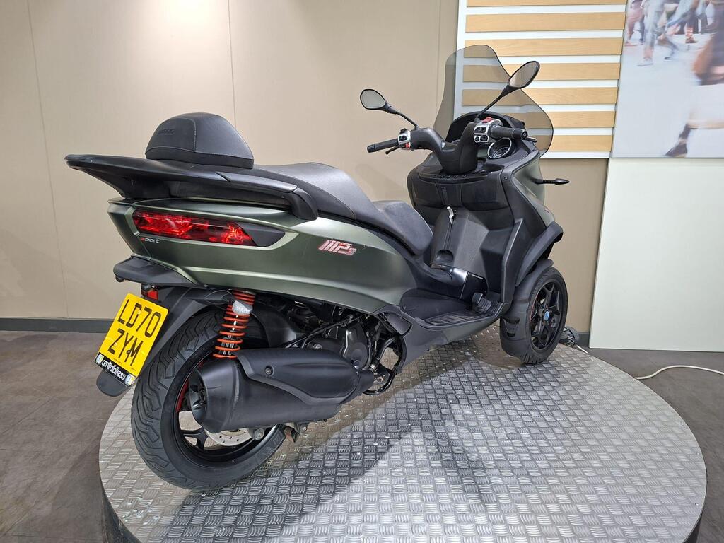 Piaggio MP3 350 LT Sport 2020 9 A three-wheeled scooter with a sleek, modern design parked on a circular platform, featuring a green body, dual rear lights, and a black seat.