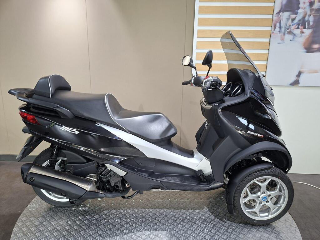 Piaggio MP3 500 Business 2021 4 A sleek black and silver three-wheeled scooter displayed in an indoor showroom setting, showcasing its modern design and features.