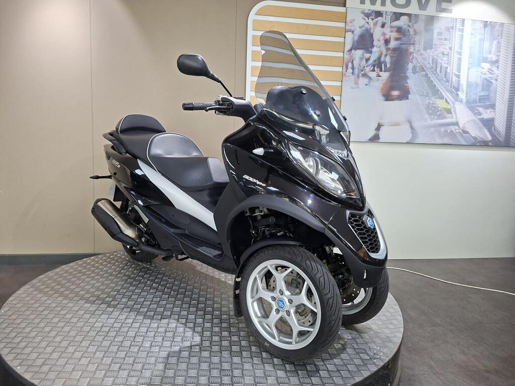 Piaggio MP3 500 Business 2021 5 A black three-wheeled scooter displayed on a circular platform against a neutral backdrop, featuring a protective windshield and a sleek design.