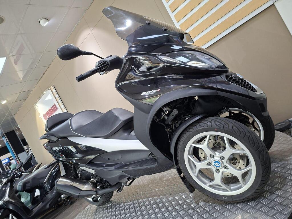 Piaggio MP3 500 Business 2021 6 A black and silver three-wheeled scooter is displayed in a dealership, showcasing its sleek design and modern features against a neutral background with showroom elements.